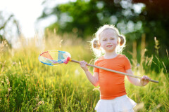 Young girl holding a butterfly net in a field of grass looks at viewer