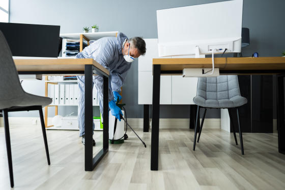 image of a man in PPC spraying bug and mouse deterrent around an empty school or office space.